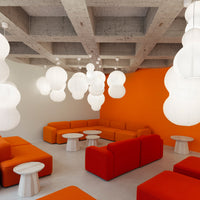 Modern lounge with vibrant orange seating, white cloud-like light fixtures, and a minimalist concrete ceiling.