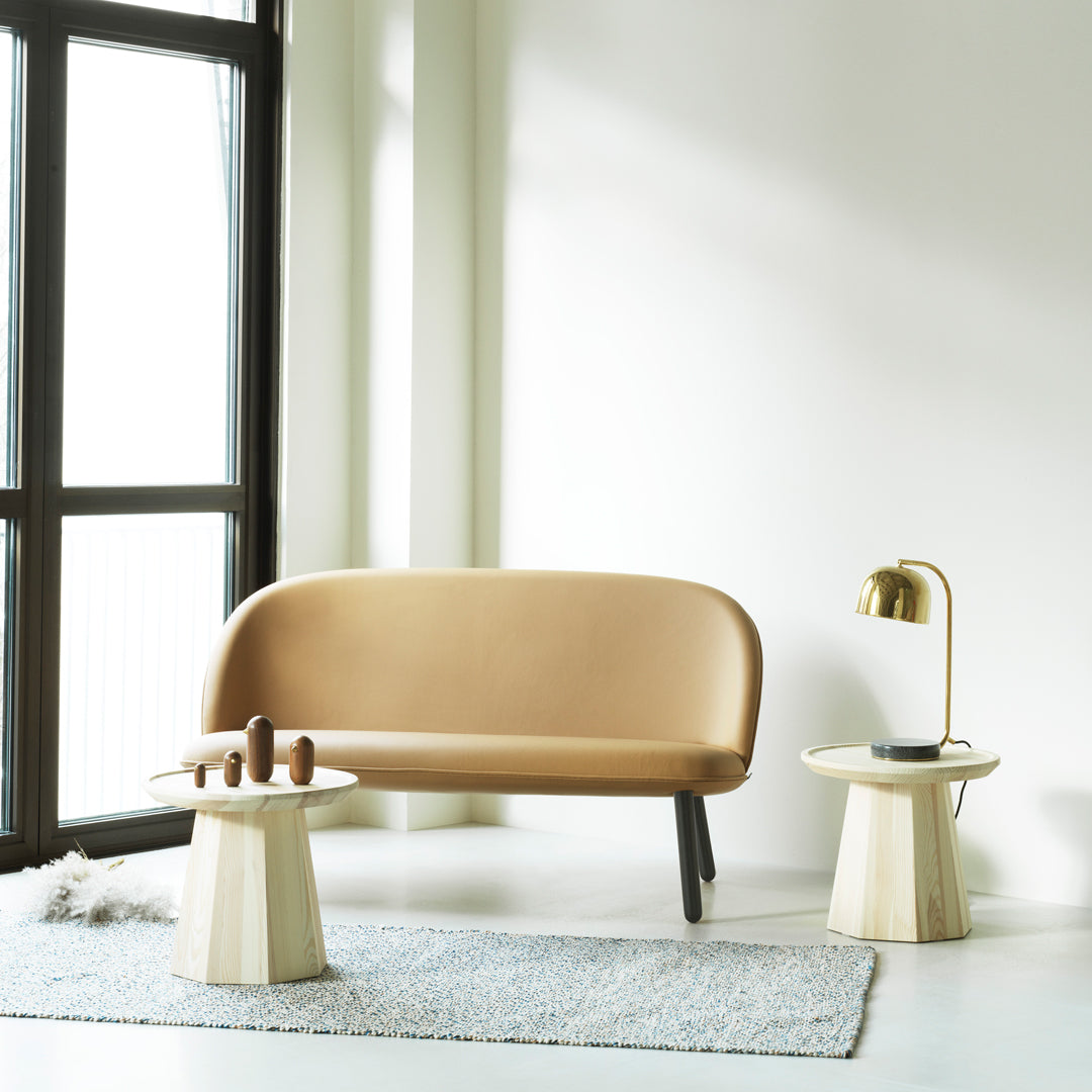 "Beige curved sofa paired with light wooden accent tables; soft gray rug enhances modern minimalist decor."