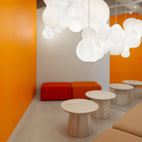 Bright orange wall with white pendant lights, red seating, and light wooden tables, creating a modern, vibrant atmosphere.