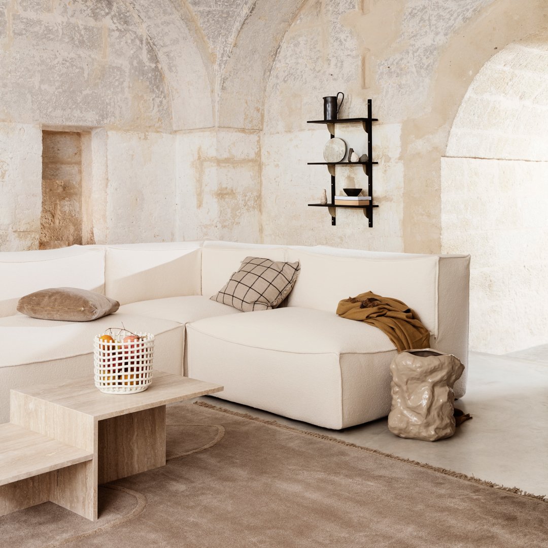 Light beige sectional sofa with a plaid cushion, paired with a neutral rug and minimalist wooden table.