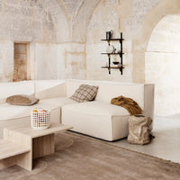 Light beige sectional sofa with a plaid cushion, paired with a neutral rug and minimalist wooden table.