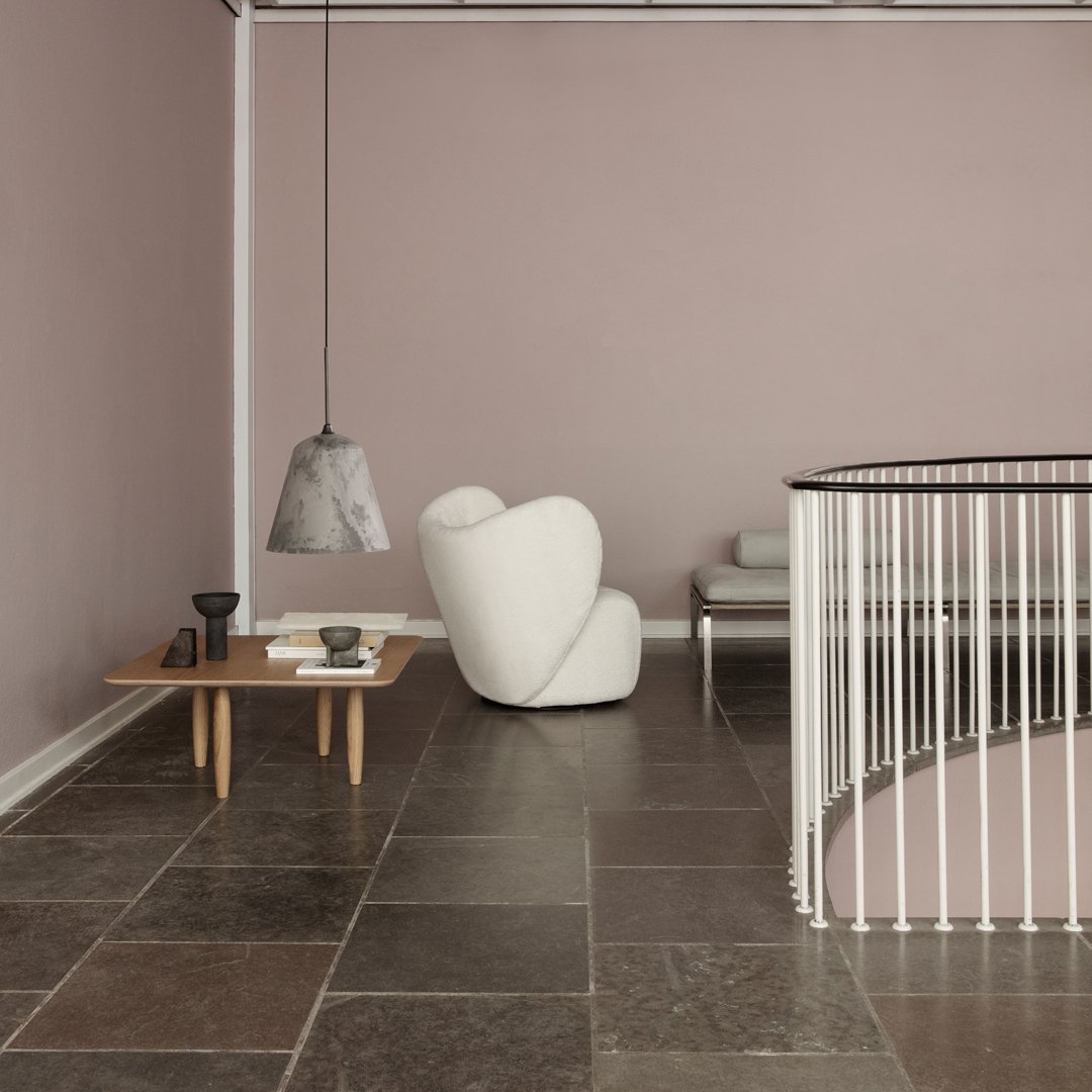 Modern interior featuring soft pink walls, gray stone flooring, and a white curvy chair against a minimalist design.