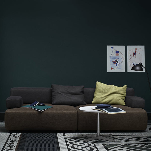 Modern dark brown sectional sofa with gray and green cushions, set against a dark green wall and patterned black and white rug.