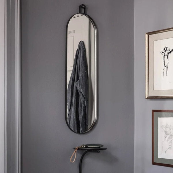 Sleek black oval mirror against a gray wall, complemented by a minimalist decor and subtle artistic accents.