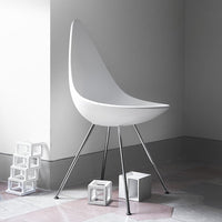 White modern chair with smooth curves and sleek metallic legs, set against a minimalist gray and pastel background.