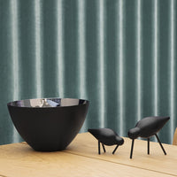 Black bowl on wooden table with glossy interior, paired with small black decorative animals against a teal vertical striped backdrop.