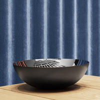 Black bowl featuring geometric patterns, placed on a wood surface, against a textured blue striped backdrop.