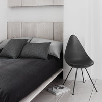 Stylish black bedspread with patterned gray pillows, complemented by a sleek black chair and neutral wood accents.