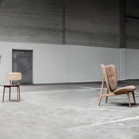 Two modern chairs: one beige and light wood, the other brown with textured fabric, set against a minimalist gray concrete background.