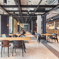 Modern cafe interior with wood and black furniture, grey flooring, and large windows letting in natural light.