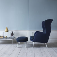 Navy blue high-back chair and matching ottoman against a light blue wall, complemented by a white wooden floor.