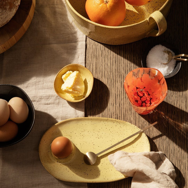 "Yellow speckled plate, vibrant orange bowl, black dish, and textured fabric create a warm, inviting dining scene."