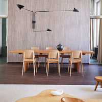 Modern dining room featuring a neutral gray wall, light wood furniture, and black lighting accents. Minimalist design.