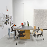 Modern dining space featuring a gray table, stacked wooden chairs in muted colors of blue, black, and natural wood.