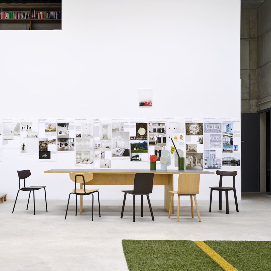 Minimalist dining room featuring a wooden table with brown, black, and light-colored chairs against a white wall.