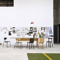Minimalist dining room featuring a wooden table with brown, black, and light-colored chairs against a white wall.