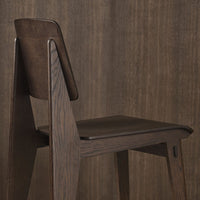 Dark wood chair with a sleek, minimalist design and a rich brown leather seat, set against a textured wooden backdrop.