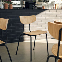 Wooden chair with natural finish and black metal legs, set against a gray tiled backdrop. Minimalist and modern design.