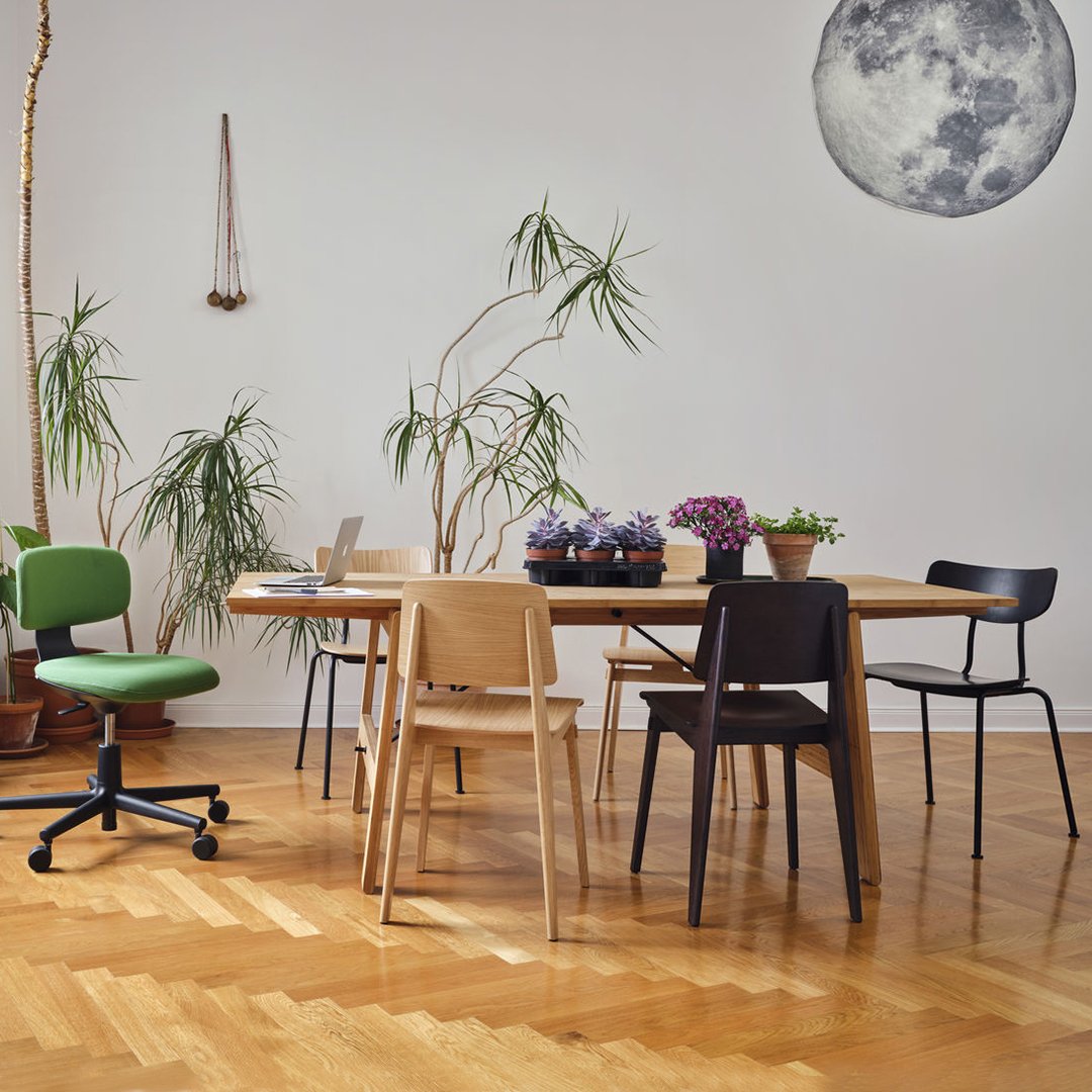 "Modern dining set featuring natural wood tones, green chair, black and light wood chairs, and vibrant purple flowers."