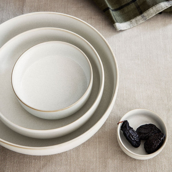 Three elegant cream bowls with subtle gold rims, arranged on a textured linen surface. Small dish with dark fruits.