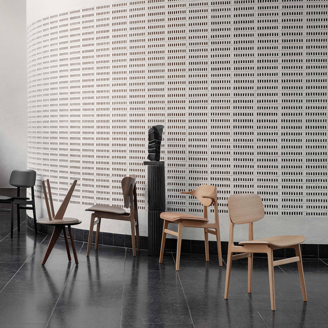 "Minimalist chairs in natural wood tones and dark finishes against a textured white wall pattern."
