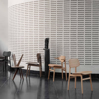 "Minimalist chairs in natural wood tones and dark finishes against a textured white wall pattern."