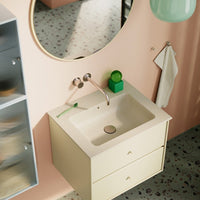 Modern bathroom sink in soft yellow with speckled countertop, complemented by pastel pink walls and green decor accents.