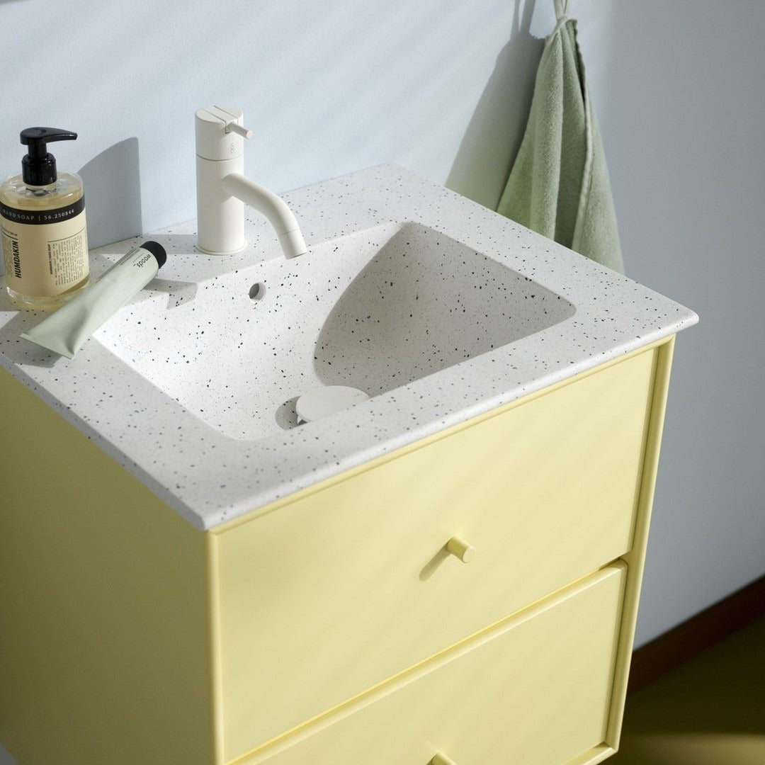 Yellow bathroom vanity with a speckled white countertop and minimalist design, complemented by green towel accents.