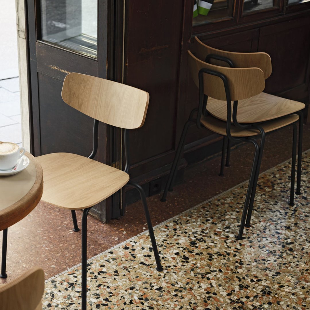 Minimalist wooden chair with a natural finish and black metal legs, set against a speckled terrazzo floor.