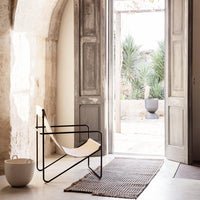 Minimalist black and cream chair, textured gray rug, natural light enhancing earthy tones and soft patterns.