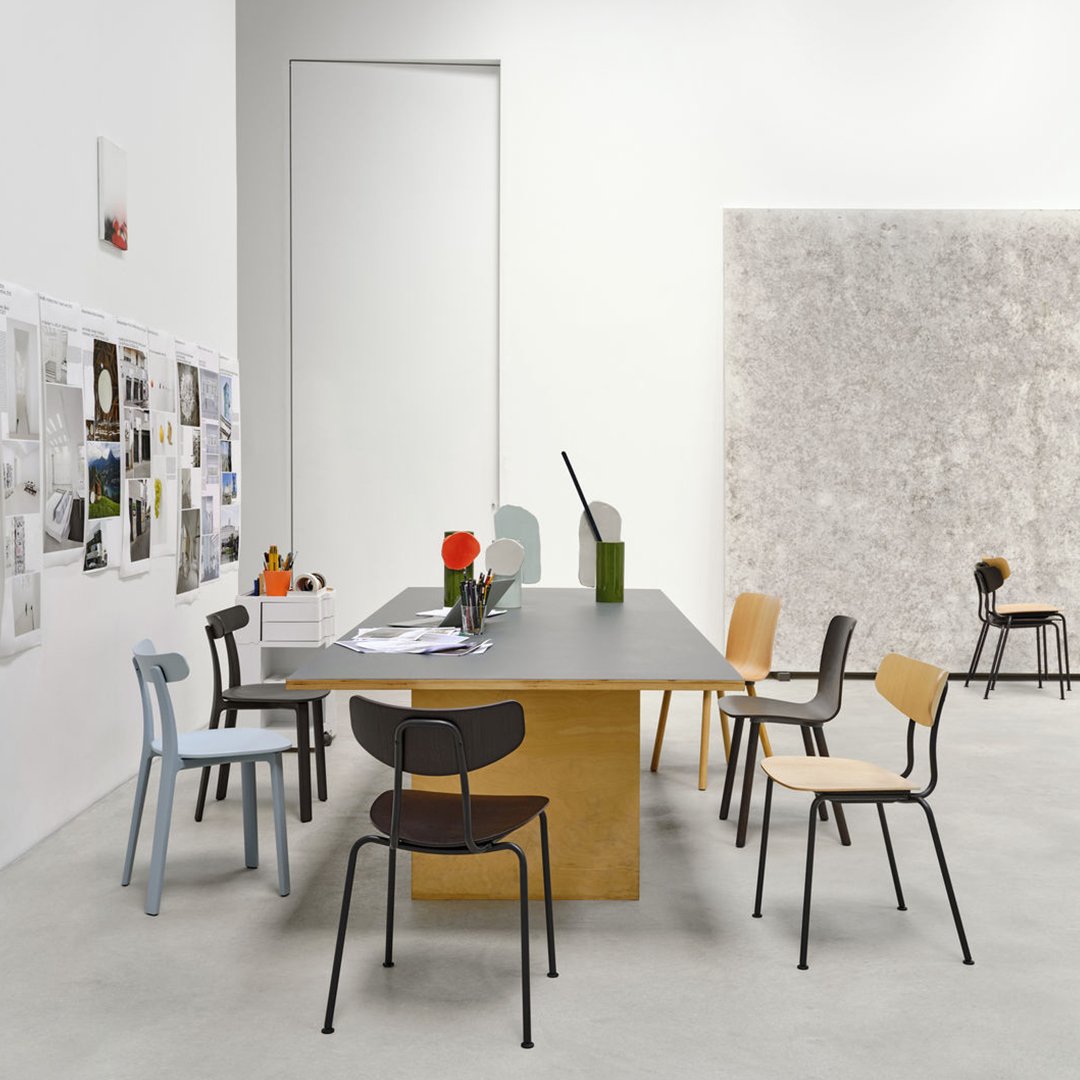 Modern workspace featuring a sleek gray table, colorful chairs in blue, black, and natural wood tones, and minimalistic decor.
