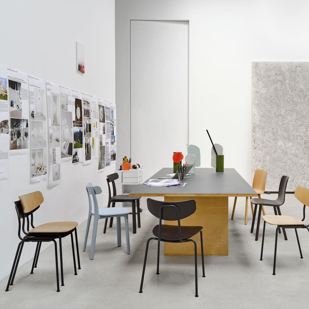 Colorful assortment of modern chairs in natural wood, black, and pale blue, set against a minimalist, neutral backdrop.