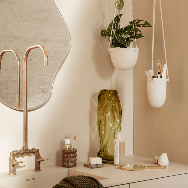 "Elegant green glass vase, white hanging planter, and neutral tones create a warm, modern aesthetic."