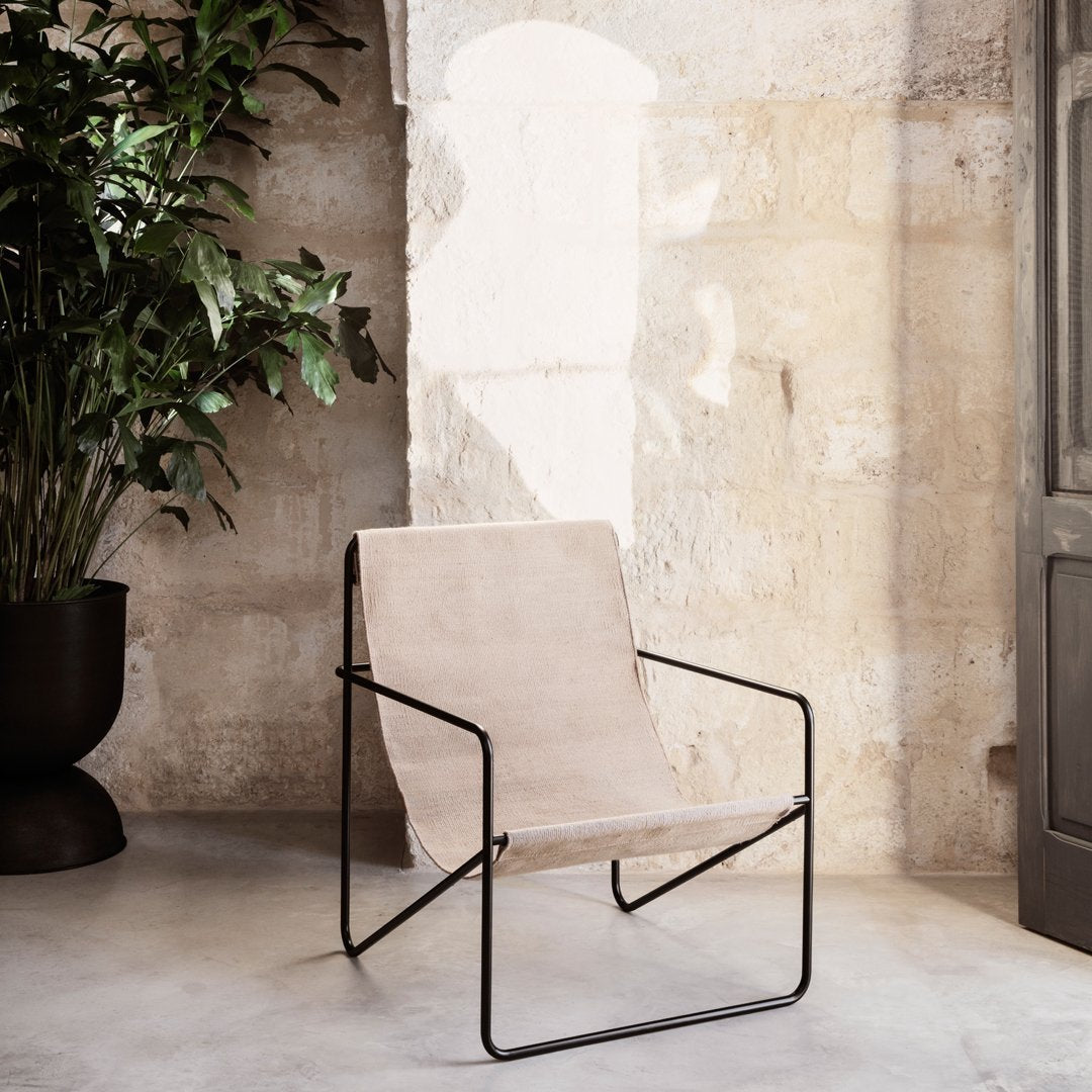 Minimalist beige chair with a sleek black metal frame against a textured stone wall. Modern and stylish design.