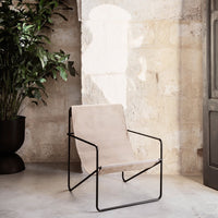 Minimalist beige chair with a sleek black metal frame against a textured stone wall. Modern and stylish design.