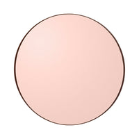 Round mirror with a soft pink surface and a sleek dark frame, adding elegance to any decor.