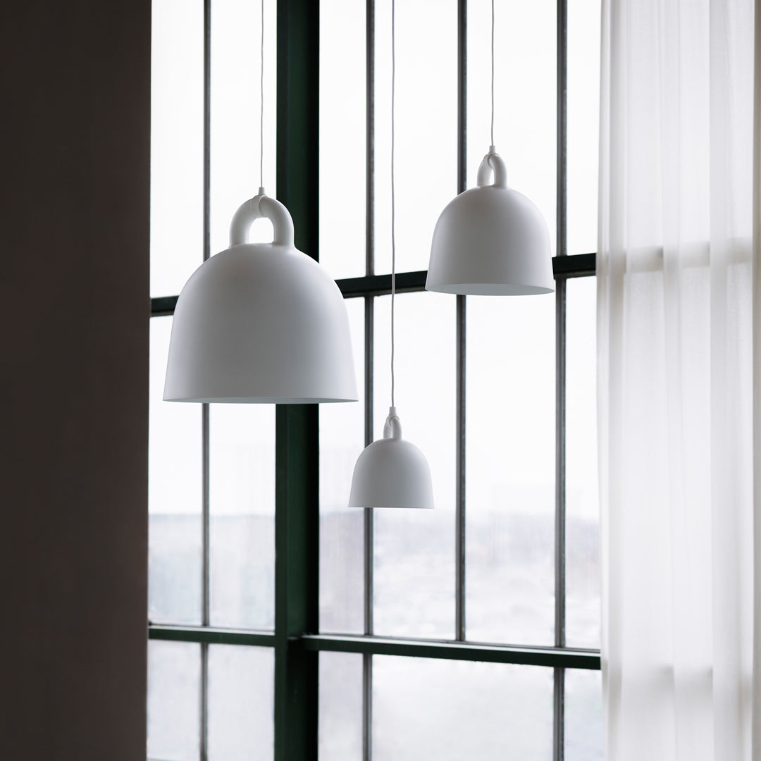 Three smooth, white pendant lamps in varying sizes against green window frames and sheer curtains.