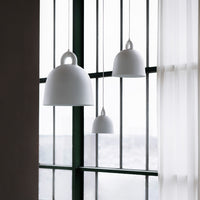 Three smooth, white pendant lamps in varying sizes against green window frames and sheer curtains.