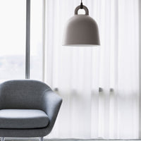 Modern gray chair under a sleek, white bell-shaped lamp, with soft white curtains in the background.