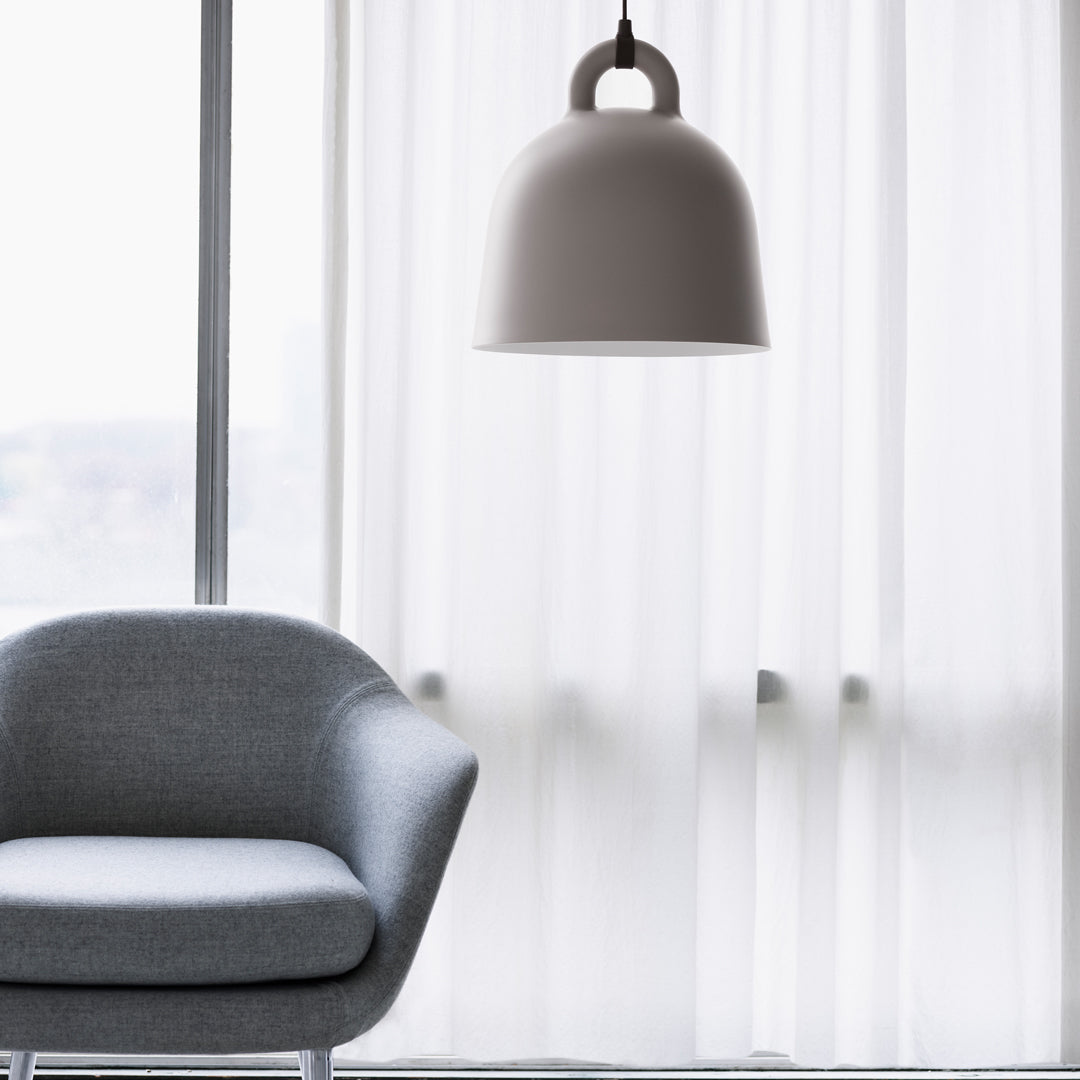 Modern gray chair under a sleek, white bell-shaped lamp, with soft white curtains in the background.