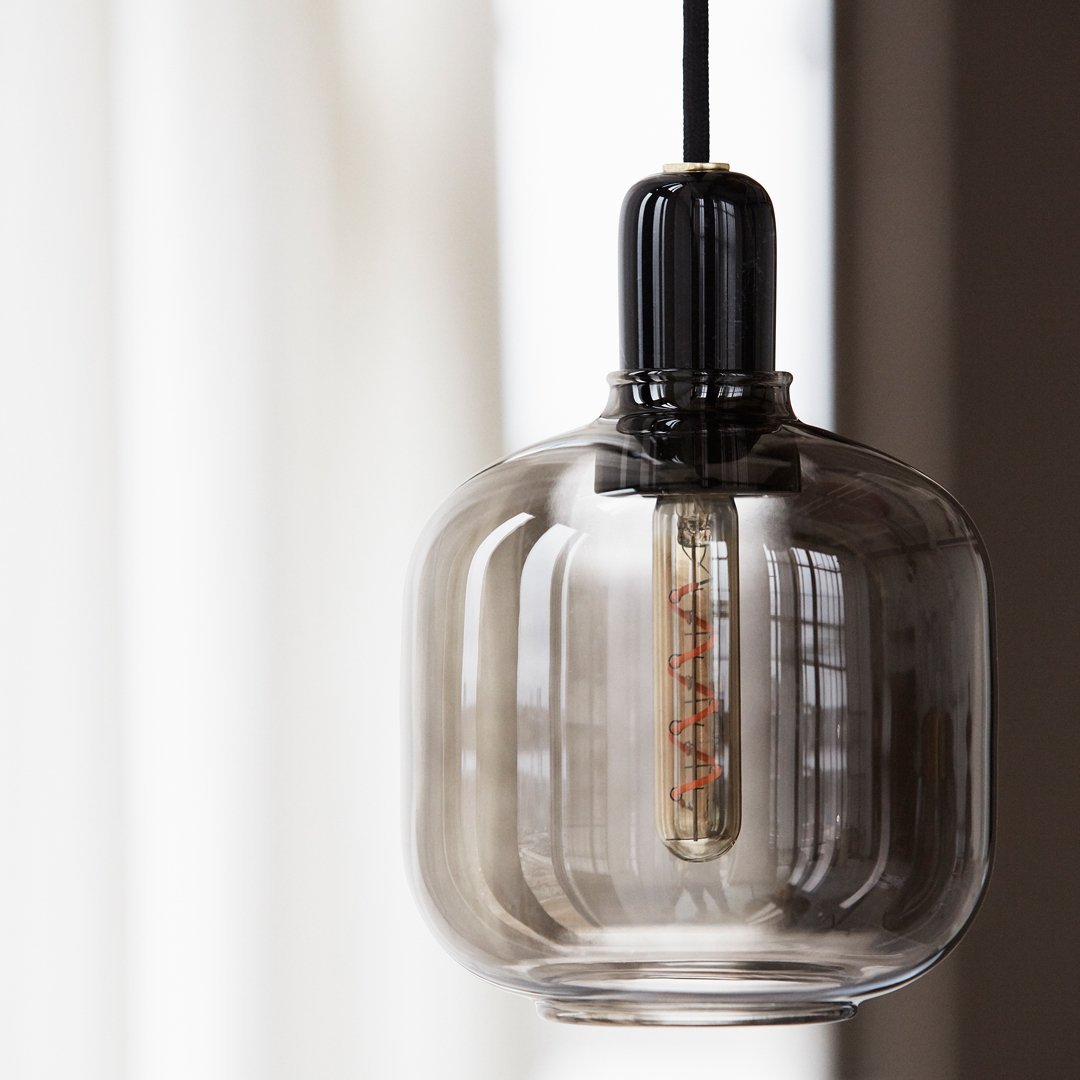 "Clear glass pendant light with a black cap and warm glowing filament, featuring smooth, rounded curves."
