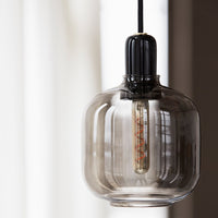 "Clear glass pendant light with a black cap and warm glowing filament, featuring smooth, rounded curves."