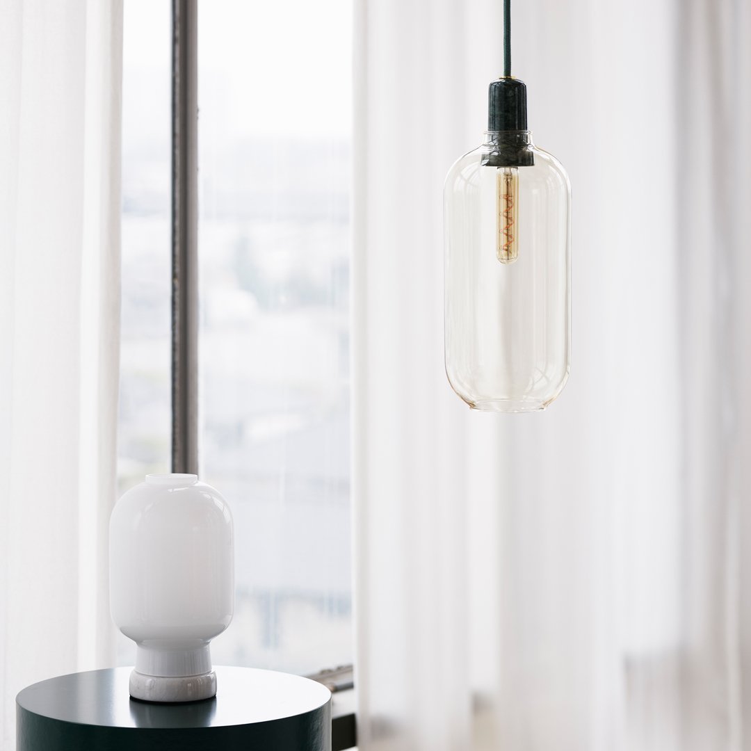 Clear glass pendant light with a sleek black cord, complemented by a smooth white lamp base and neutral curtains.