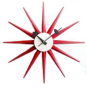 Red starburst clock with sharp, pointed rays and a white round face. Modern design with black hour and minute hands.
