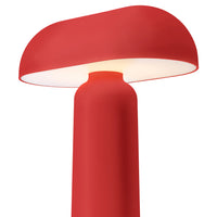 Red modern lamp with a smooth, rounded shade and a sleek cylindrical base, emitting a warm glow.