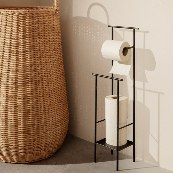 Black metal paper towel holder with a minimalist design, set against a beige wall and a textured wicker basket.