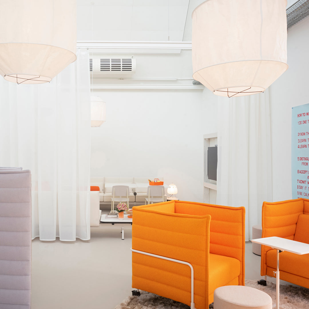 Bright orange lounge chairs with a modern design against a white backdrop, featuring soft lighting and elegant curtains.
