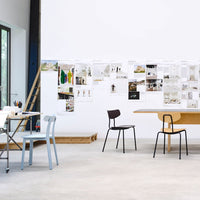 Modern workspace featuring a light blue chair and a sleek black chair against a minimalistic white wall and wooden table.