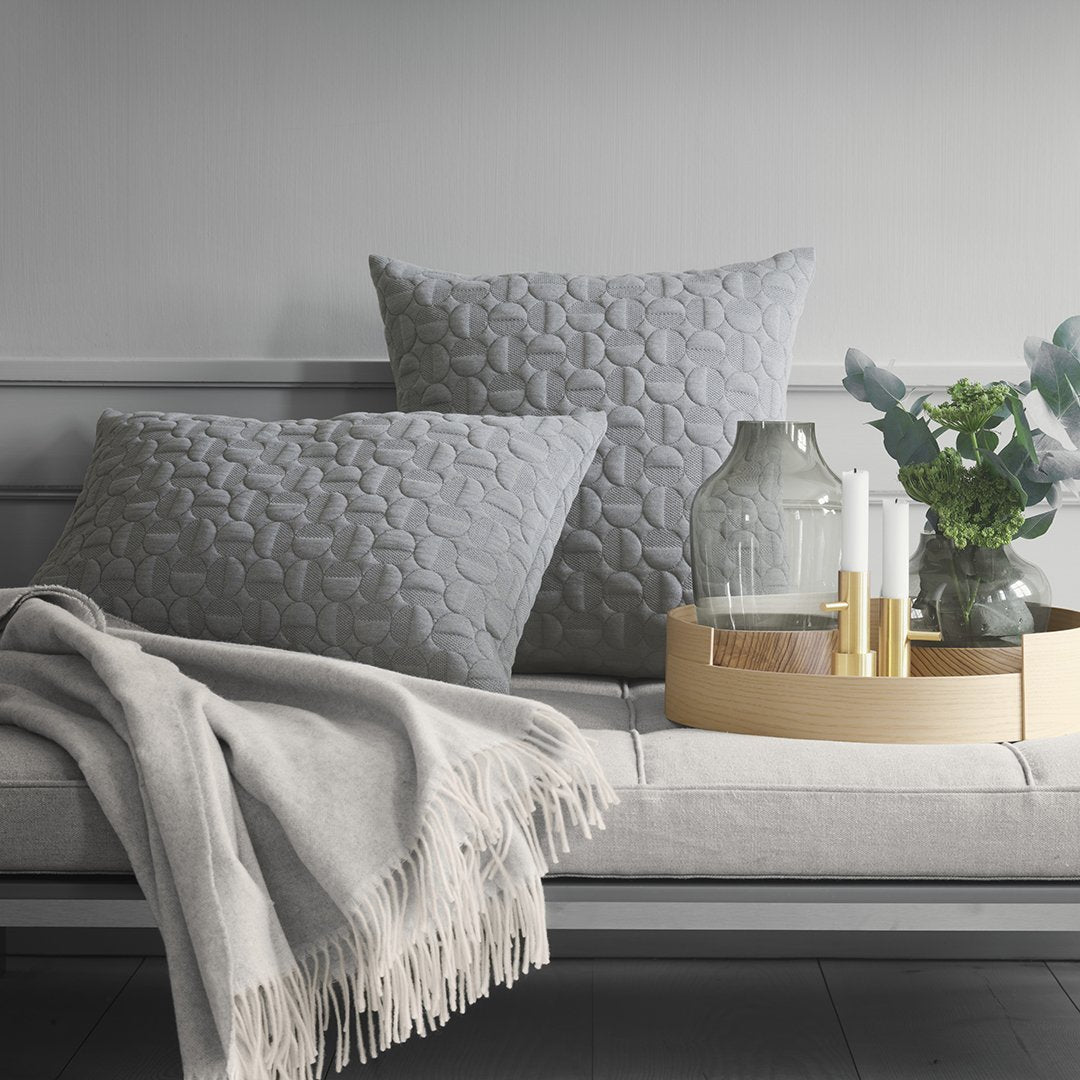 Gray textured throw pillows with a subtle pattern, paired with a light gray blanket and neutral decor elements.