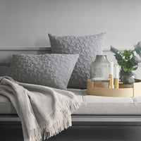 Gray textured throw pillows with a subtle pattern, paired with a light gray blanket and neutral decor elements.
